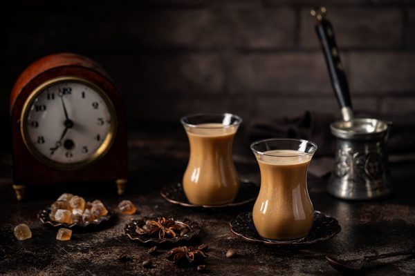 Tea or Coffee with milk and spices in glass Armudu with coffee beans and sugar on dark background.